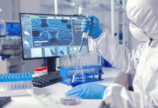 Virolog coducting experiment in the course of coronavirus pandemic with micropipette. Chemist in modern laboratory doing research using dispenser during global epidemic with covid-19.